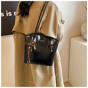 Détail d'un sac cabas en cuir noir brillant avec logo doré et pendentif tressé élégant
