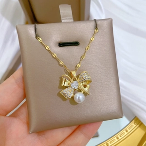 Macro shot of gold bow pendant with sparkling zircons and a white pearl on a wave chain