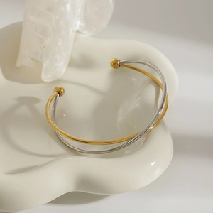 Detail of a minimalist gold and silver intertwined open bangle with spherical ends