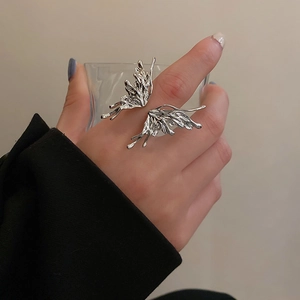 Detail of silver liquid metal butterfly wing open ring worn while holding a glass