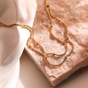 Minimalist double-layered gold snake chain necklace with beads on soft white satin and stone