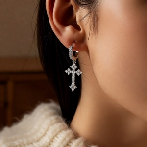 Close-up of silver cross hoop earring with white zircons worn by model in warm lighting