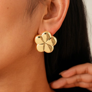 Close-up of a polished gold flower stud earring worn by a model in a minimalist style