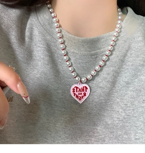 Close-up of pearl necklace featuring a pink heart pendant with That's All Right text