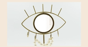 Detailed view of eye-shaped gold jewelry stand with central mirror and pearl bracelet