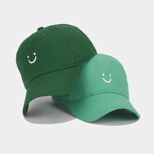 Close-up of cotton baseball caps in dark and light green with smiley face embroidery