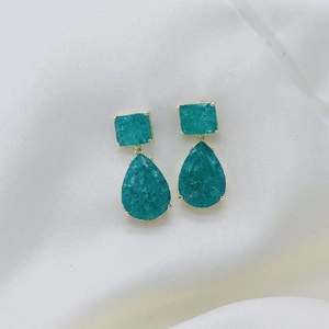 Close-up of teardrop green gemstone earrings with gold frames on silk fabric
