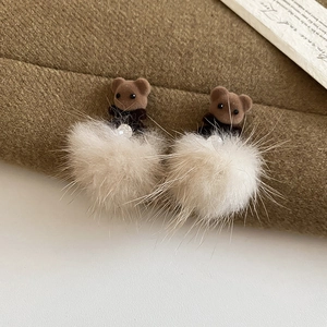 Close-up of brown flocked bear earrings with soft white fur pom-poms for winter style