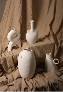 Close-up of four matte white ceramic vases with abstract shapes and textured finish