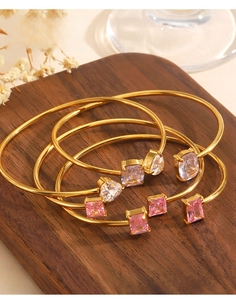 Detail of gold-plated stainless steel bangles with colorful zircon gemstones on wood