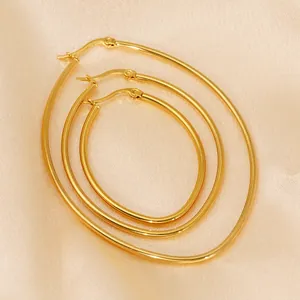 Three pairs of oval gold stainless steel hoop earrings on light beige satin background