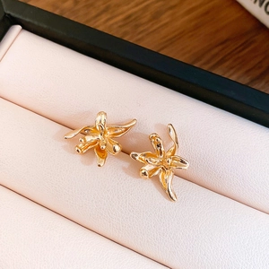 Close-up of golden metallic flower stud earrings resting in a pink textured jewelry box