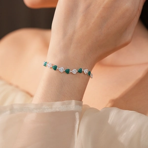 Detail of a silver heart bracelet with green enamel and white zircon on a woman's wrist