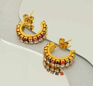 Macro de boucles d'oreilles C dorées à l'or 18 carats avec zircons colorés sur surface miroir