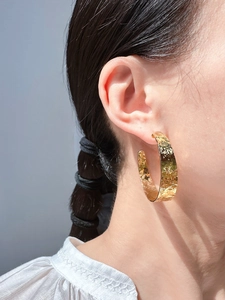 Detail of large gold C-shape hoop earrings with hammered crinkle texture on model