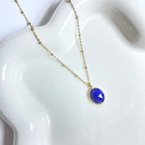 Detail of a 14K gold-plated beaded chain necklace with an oval blue gemstone pendant