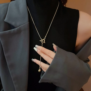 Detailed view of long gold snake chain necklace with OT buckle and round metal ball pendant
