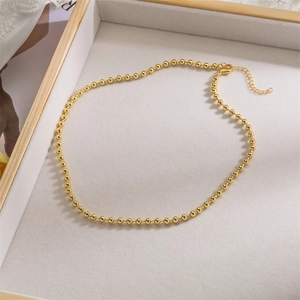 Detailed shot of a gold beaded necklace with adjustable extension chain on beige tray
