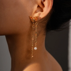 Macro detail of long butterfly earrings with orange zircon, metal fringe and pearl