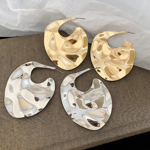 Macro shot of large C-shaped earrings with gold and silver hammered metal textures