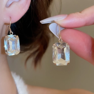 Detailed view of elegant gold-toned hook earrings featuring a sparkling square-cut crystal gem