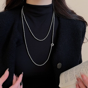 Detail of silver double-layered beaded necklace with flower charm on black tweed jacket