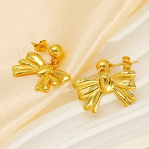 Golden bow-shaped stainless steel earrings with sparkling zircons on beige silk background