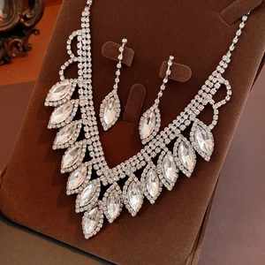 Close-up of sparkling crystal waterdrop tassel earrings and necklace on brown velvet stand