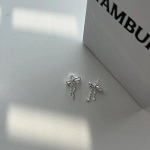 Detail of silver bow earrings with long chain tassels showing polished metal texture
