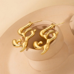 Macro shot of abstract wavy golden earrings with high-polish finish on a ceramic stand