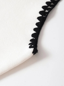 Makroaufnahme von weißem Strickstoff mit schwarzer gewellter Häkelborte und Textur