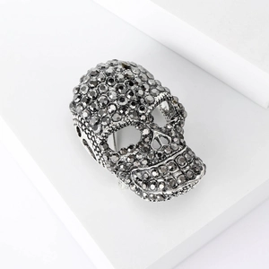 Close-up of a skull brooch set with dark faceted rhinestones on a white geometric stage
