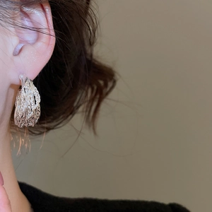 Detail view of silver earring featuring unique crumpled texture on model ear