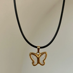 Detail of 18k gold butterfly necklace featuring white pearlescent inlay and black rope