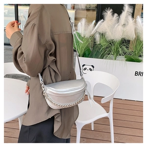 Silver metallic saddle bag with chain detail shown on shoulder in outdoor setting