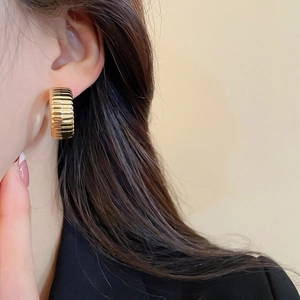 Close-up of a model wearing a chunky gold wrinkled texture hoop earring in retro style