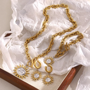 Detailed close-up of 18K gold sun pendant necklace and earrings on a wooden tray
