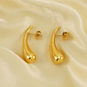 Macro shot of 18K gold teardrop stud earrings with a polished mirror finish on silk fabric