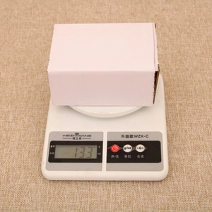Glow Christmas resin ornament house in a plain white box weighed on a digital scale