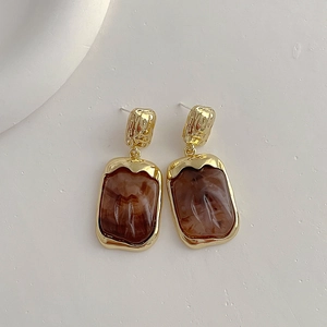 Detail of geometric earrings with brown marble resin and hammered gold metal finish