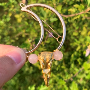 Detailansicht einer Mondsichel-Haarspange mit goldenem Krähenschädel und Rosa Perlen