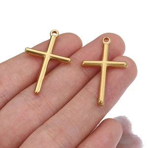 Golden stainless steel cross pendant shown on fingertips for size and scale reference