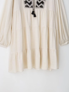 Detail of bohemian embroidery and black tassel ties on ivory tiered dress fabric