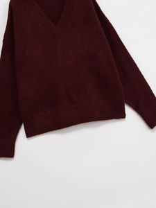 Detailed view of maroon V-neck knitted sweater with ribbed cuffs on white background