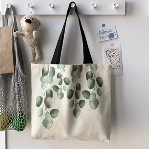 Detail of canvas tote bag featuring green eucalyptus leaves and black handles