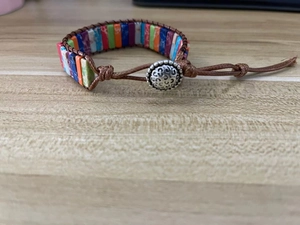 Detail of bohemian woven leather bracelet with multi-colored square stone beads and metal clasp