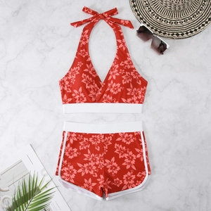 Flat lay of red hibiscus print halter bikini set with white trim on marble background