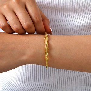Close-up of golden infinity braid bangle with a high-polish finish on a woman's wrist