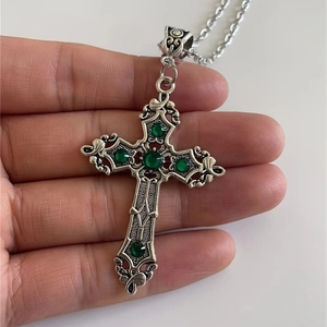 Close-up of gothic silver cross pendant featuring a polished green gemstone on a metal chain