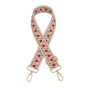 Close-up of adjustable beige canvas strap with red geometric patterns and gold metal clips